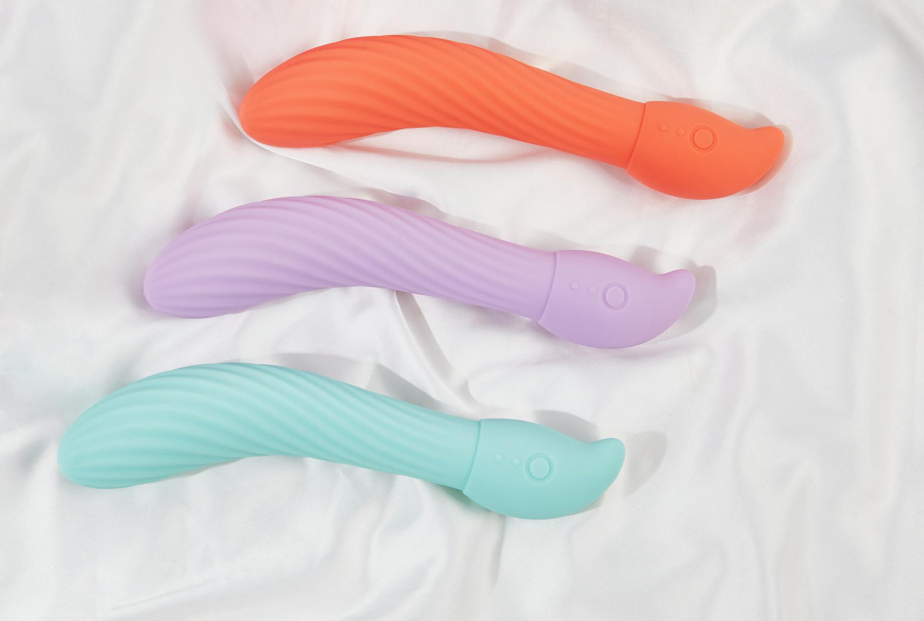 A hand holding an orange vibrator against a minimalistic purple backdrop