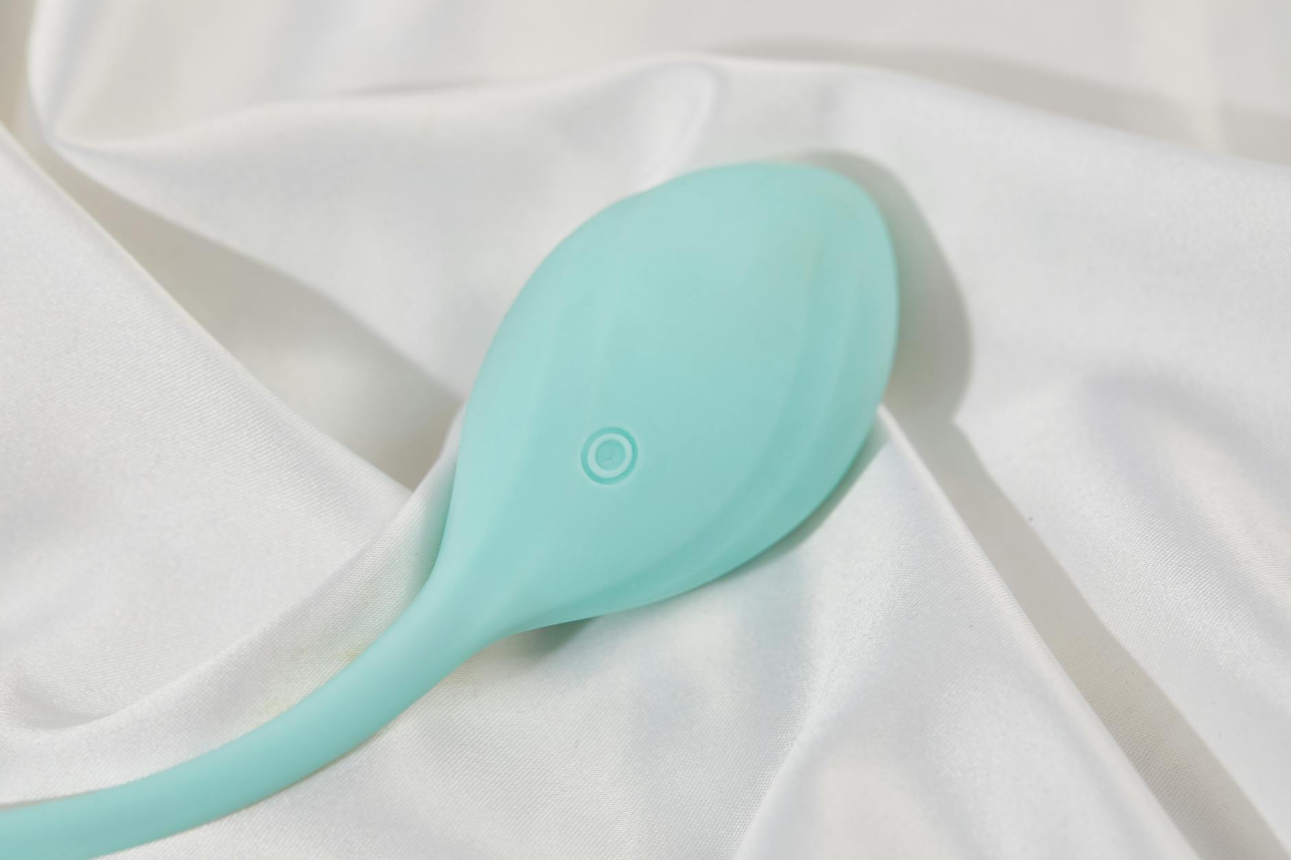 A sleek teal lemon vibrator on white silk fabric, representing post-recovery intimacy