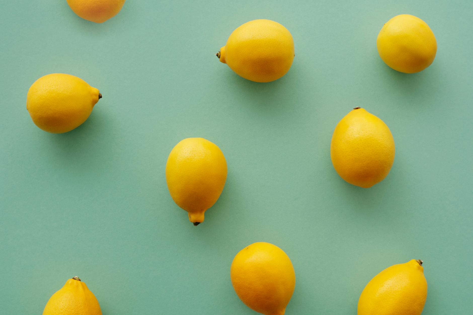 Fresh bright yellow lemons arranged on a soft pastel green background