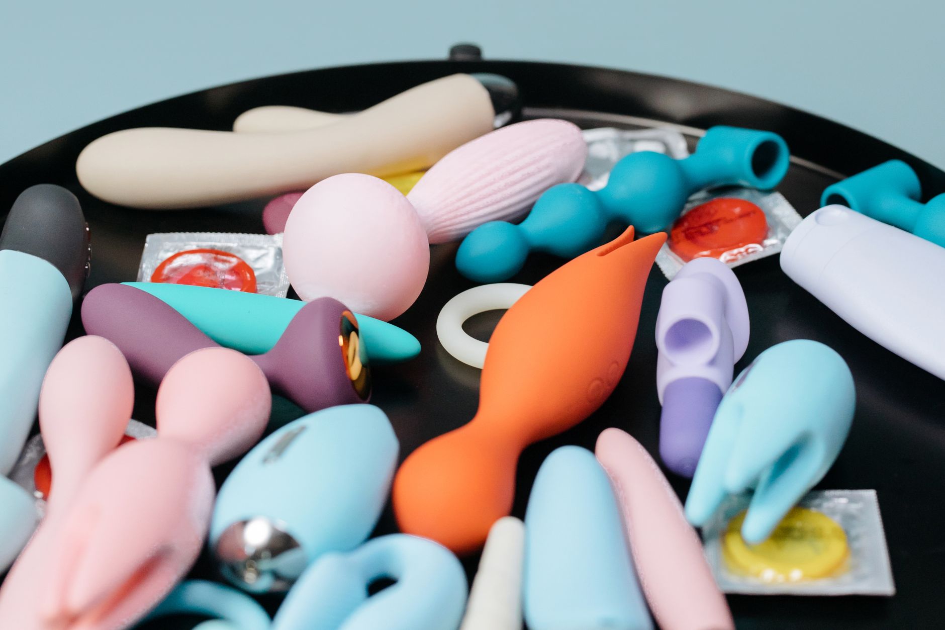 Two hands holding colorful silicone vibrators against a pastel background