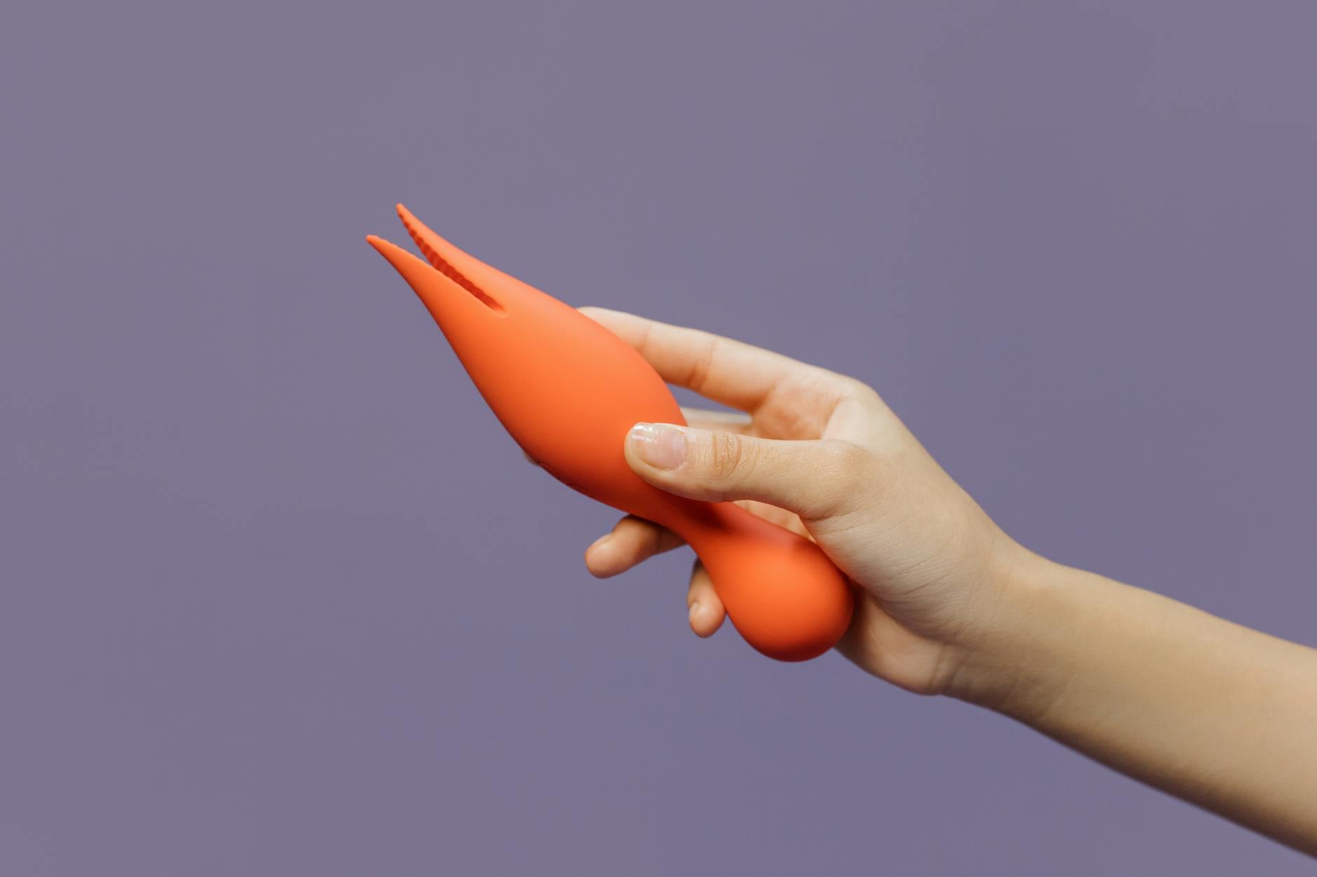 Close-up of a hand holding a lemon-colored vibrator against a minimalistic purple backdrop, showcasing modern sensual design.