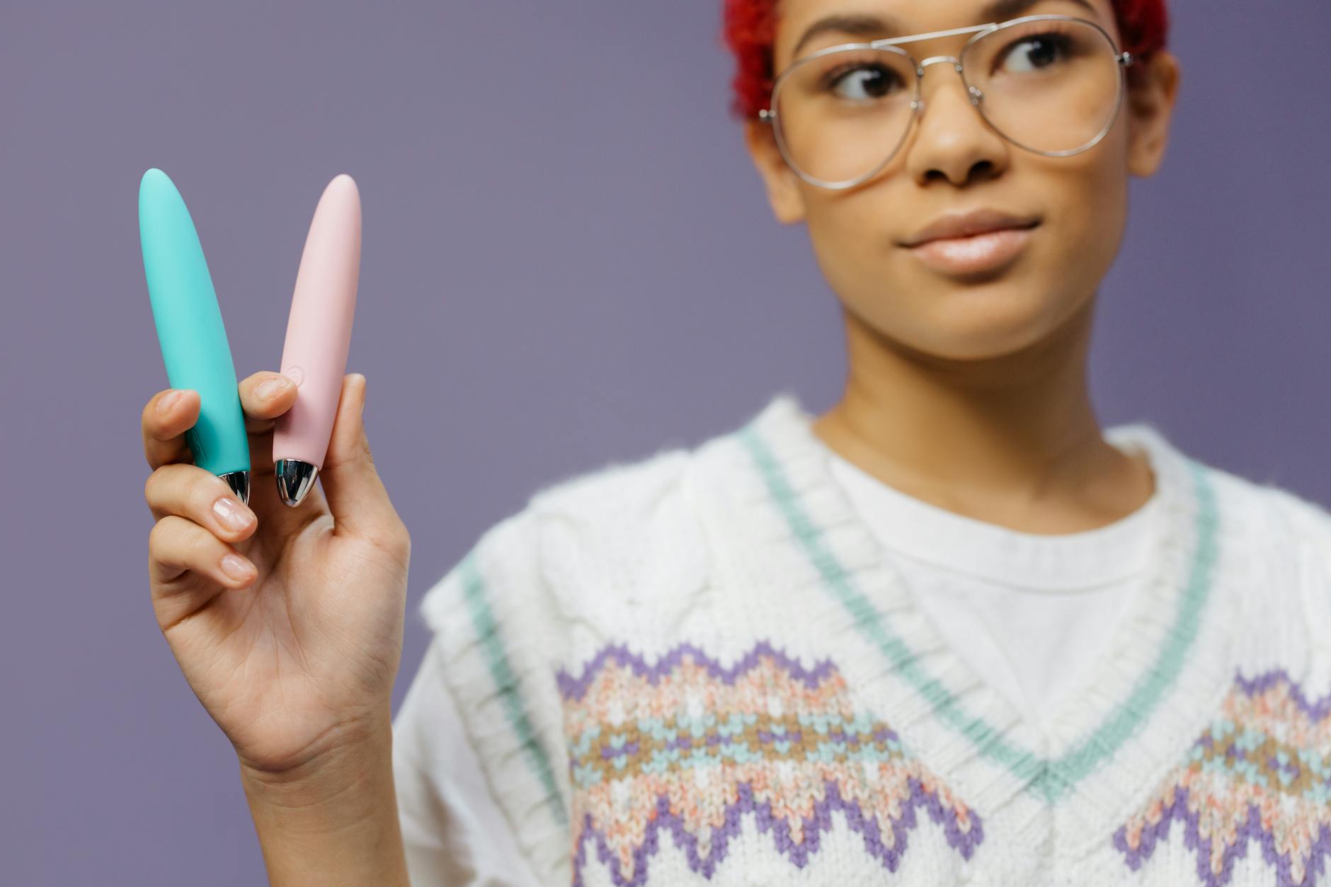 Woman holding colorful vibrators against purple background, representing exploration and self-discovery