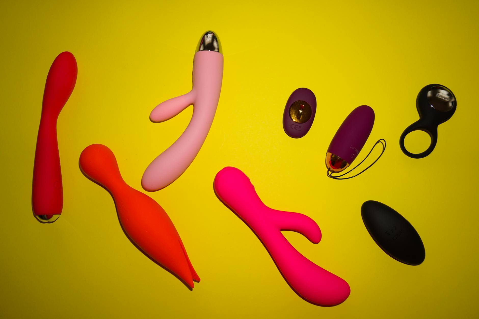 Vibrant photo of various sex toys arranged on a bright yellow surface, showcasing diversity and design